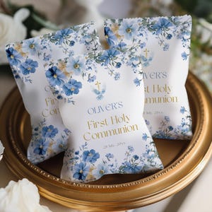 Puede incluir: Tres bolsas de recuerdo blancas con diseños florales azules y texto dorado que dice "OLIVER'S First Holy Communion". Las bolsas están en una bandeja con borde dorado. Las bolsas tienen una cruz y un gráfico de paloma.