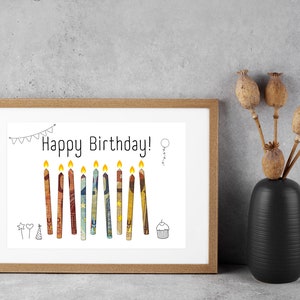 May include: A framed print with a white background and the text "Happy Birthday!" in black. The print features a row of 11 colorful candles with yellow flames.