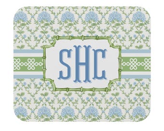 May include: A rectangular mousepad featuring a floral pattern with blue hydrangeas and green leaves. The center has a white space with the letters "SHC" in blue, framed by a green bamboo-style border.