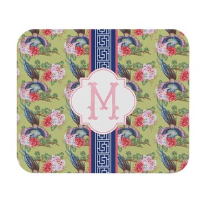 May include: A decorative mousepad featuring a repeating pattern of blue and teal birds, pink flowers, and green foliage on a light green background. A white quatrefoil shape with a pink "M" and a navy blue and white border is centered on the mousepad.