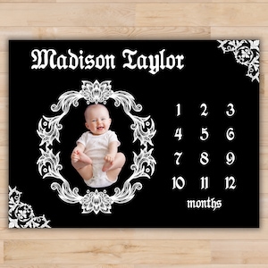 May include: Black and white baby milestone growth chart with a white ornate frame and a baby girl in the center. The chart has numbers 1 through 12 and the text "Madison Taylor" and "months".
