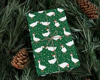 May include: A wrapped gift with green wrapping paper featuring a pattern of white geese wearing Santa hats. The gift is tied with twine and rests on a bed of pine needles and pine cones, creating a festive holiday scene.