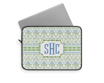 May include: Laptop sleeve with a floral pattern in light blue and green. The design includes a central rectangular frame with the initials "SHC" in blue. A silver laptop is partially visible.