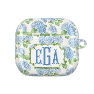 Könnte beinhalten: Weißes AirPod-Case mit blauem Hortensien-Blumenmuster. Das Case zeigt die Initialen "EGA" in blauer Schrift, umrahmt von einem grünen Bambus-Stil-Rand. Es hat eine Schlaufe zum Anbringen an einem Schlüsselanhänger.