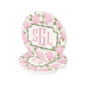 May include: Two white car coasters with a pink floral hydrangea design. Each coaster features a pink monogram within a green bamboo-style frame. The coasters are designed to fit in a car's cup holder.