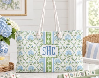 May include: A rectangular tote bag featuring a blue and green hydrangea floral pattern with white rope handles. A central vertical green and blue stripe includes a bamboo-style frame containing the blue embroidered monogram letters SHC.