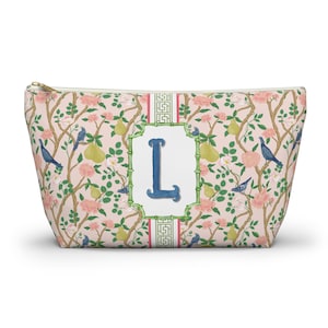 Könnte beinhalten: Eine Reißverschlusstasche mit einem floralen Muster aus rosa Rosen, Birnen und blauen Vögeln auf hellrosa Hintergrund. Die Tasche hat einen großen blauen Buchstaben "L" in einem weißen und grünen Rahmen.