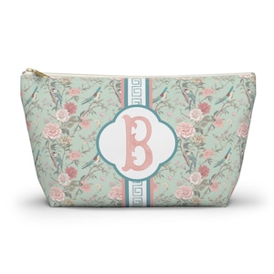 May include: A zippered cosmetic bag with a floral pattern in shades of green, pink, and blue. The bag features a white and pink initial "B" on the front, with a teal and white stripe design.