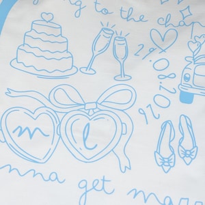 May include: White t-shirt with light blue illustrations of a wedding cake, champagne glasses, hearts, a car, shoes, and the text "going to the chapel" and "Emma get married". Includes the date 29.08.2020.