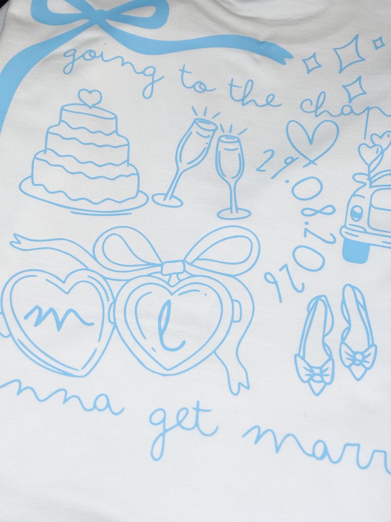 May include: White t-shirt with light blue illustrations of a wedding cake, champagne glasses, hearts, a car, shoes, and the text "going to the chapel" and "Emma get married". Includes the date 29.08.2020.