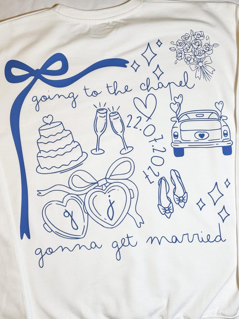 May include: White sweatshirt with blue line art. The design includes a bow, cake, champagne glasses, a car, hearts, shoes, and the phrases "going to the chapel" and "gonna get married".