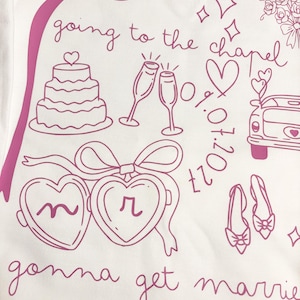 May include: White t-shirt with a pink illustration of wedding-related graphics. The design includes a cake, champagne glasses, hearts, a car, shoes, and the text "going to the chapel" and "gonna get married".