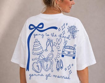 May include: White t-shirt with a blue graphic design featuring wedding-themed illustrations and text. The design includes a cake, champagne glasses, a car, and the words "going to the chapel" and "gonna get married."