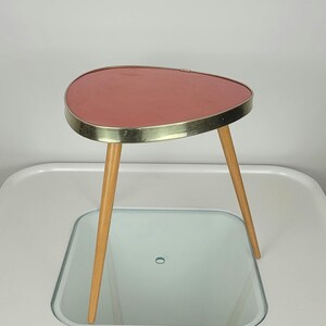May include: A pink, oval-shaped side table with a gold rim and three wooden legs.