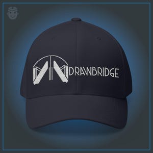 Może przedstawiać: Granatowa czapka bejsbolówka z białym haftem "DRAWBRIDGE". Czapka ma z przodu stylizowane białe logo. Klasyczny sześciopanelowy design z zakrzywionym daszkiem.