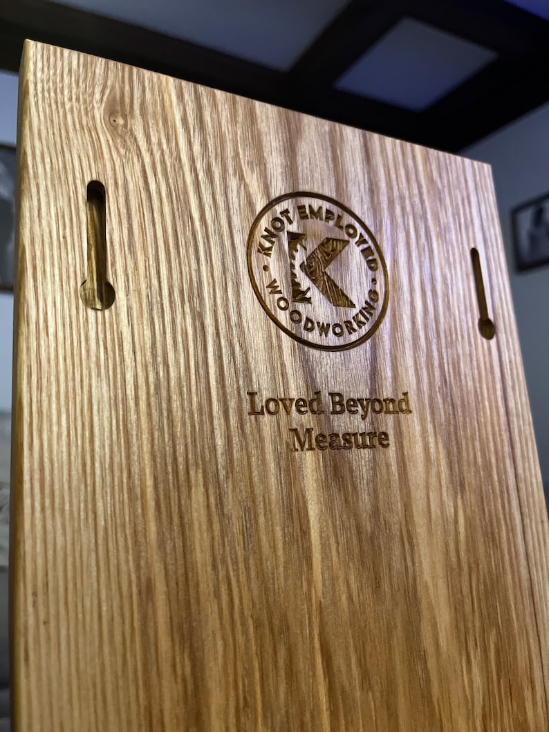 May include: Wooden plaque with the text "Loved Beyond Measure" and a circular logo that reads "Knot Employed Woodworking". The plaque has two keyhole slots for hanging and a natural wood grain finish.