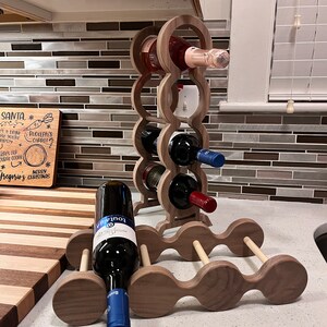 May include: A wooden wine rack with a light brown finish. The rack is made of two pieces, one tall and one short. The tall piece has five circular openings for bottles, and the short piece has three circular openings. There are six bottles of wine in the rack, including a bottle of rose wine and a bottle of red wine.