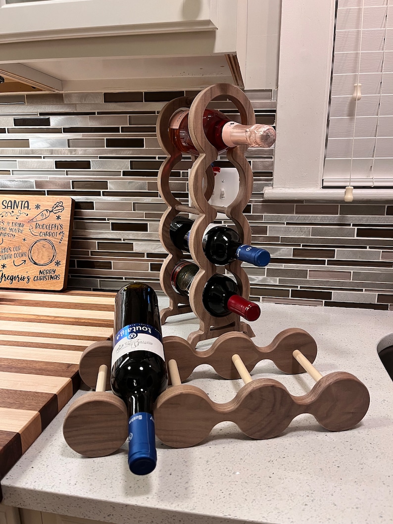 May include: A wooden wine rack with a light brown finish. The rack is made of two pieces, one tall and one short. The tall piece has five circular openings for bottles, and the short piece has three circular openings. There are six bottles of wine in the rack, including a bottle of rose wine and a bottle of red wine.