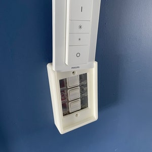 May include: A white light switch with four buttons. The top button has an icon of a light bulb, the second button has an icon of a sun, the third button has an icon of a star, and the bottom button has an icon of a circle. The switch is labelled "PHILIPS".