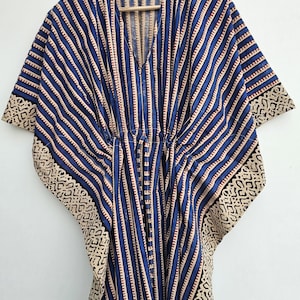 May include: A blue and white striped kaftan dress with a V-neck and a drawstring waist. The sleeves and hem feature a beige and black geometric pattern. The garment is hanging on a wooden hanger.