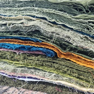 Pode incluir: Uma pilha de papel artesanal em várias cores, incluindo verde, azul, laranja e roxo. As bordas do papel são desfiadas, dando-lhe uma aparência texturizada. O papel é provavelmente usado para projetos de arte ou artesanato.