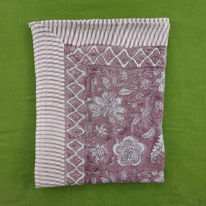 Könnte beinhalten: Ein rosa-weißer Baumwollstoff mit einem Blumendruck. Der Stoff hat einen weißen Rand mit rosa Streifen und einen rosa Rand mit einem Blumenmuster.