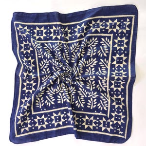 Könnte beinhalten: Ein quadratisches, marineblaues Bandana mit einem cremefarbenen, sich wiederholenden Blatt- und Sternmuster. Das Design wird von einem Rand aus cremefarbenen Sternen und geometrischen Formen umrahmt. Der Stoff ist in der Mitte gefaltet.