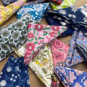 May include: A collection of colorful fabric squares with various floral and geometric patterns. The squares are folded and arranged on a wooden surface.