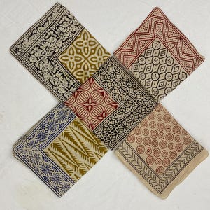 Op de afbeelding: Set van vier katoenen vierkanten met verschillende blokgeprinte patronen in tinten bruin, rood, blauw en zwart op een crème achtergrond.