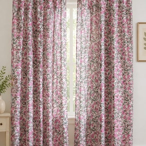 Könnte beinhalten: Ein Paar bodenlange Vorhänge mit einem sich wiederholenden Blumenmuster aus rosa Blüten und dunkelgrünem Blattwerk auf weißem Grund. Die Vorhänge sind mit Stoffschlaufen an einer Metallstange befestigt, was einen gefalteten Fall erzeugt.
