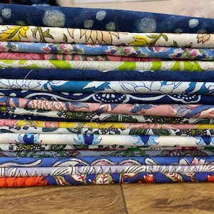 Könnte beinhalten: Ein Stapel bunter Stoffe mit Blumenmustern. Der Stoff ist ordentlich gefaltet und hat eine Vielzahl von Farben, darunter Blau, Rosa, Grün und Gelb.