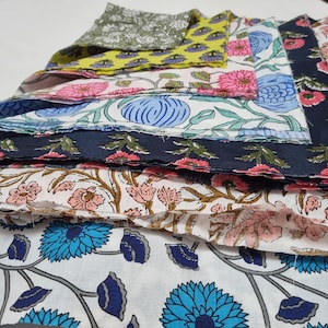 Może przedstawiać: Stos wzorzystych próbek tkanin z kwiatowymi wzorami w różnych kolorach. Wzory obejmują różowe, niebieskie i zielone kwiaty na białym, żółtym i granatowym tle. Tkaniny są warstwowe, prezentując różne wzory.