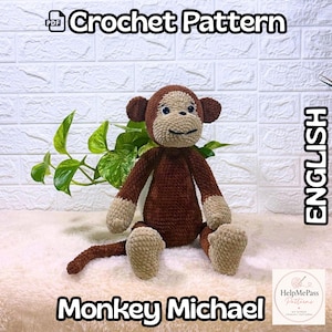 Könnte beinhalten: Ein gehäkeltes Affenspielzeug in Braun- und Beigetönen, mit dem Text "Crochet Pattern" und "Monkey Michael". Das Spielzeug hat ein lächelndes Gesicht und sitzt mit ausgestreckten Beinen. Das Wort "English" ist ebenfalls sichtbar.
