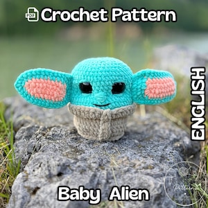 Può includere: Una figura di Baby Alien all'uncinetto, con grandi orecchie, nei toni del turchese, pesca e grigio. La figura ha grandi occhi neri ed è seduta su una roccia. Le parole "Crochet Pattern" e "Baby Alien" sono visualizzate.