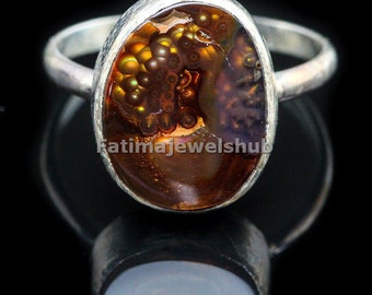 May include: A silver ring with a brown agate gemstone. The agate has a unique pattern of brown, orange, and gold swirls. The ring is set in a silver band.