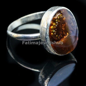 May include: A silver ring with a large oval-shaped agate gemstone. The agate is brown with a pattern of small, dark brown and gold inclusions. The ring is set in a silver band.