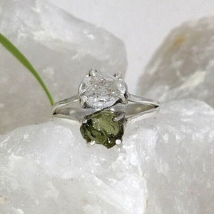 May include: A silver ring with a clear, rough-cut gemstone and a green, rough-cut gemstone.