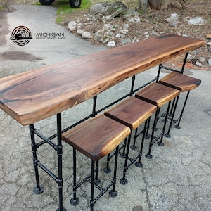 May include: A rustic wooden bar with four matching stools. The bar top and stool seats are made of dark brown wood. The bar and stools have black metal pipe legs. The bar is long and rectangular, with a live edge.