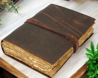 Può includere: Un diario in pelle marrone con chiusura a cinturino. Le pagine hanno un aspetto vintage e invecchiato. Il diario è su una superficie di legno con elementi decorativi.