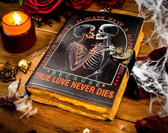 Op de afbeelding: Zwart lederen dagboek met een skeletpaarontwerp. Het dagboek heeft een metalen sluiting en de tekst "Liefde heeft niet altijd een happy end... want ware liefde sterft nooit."