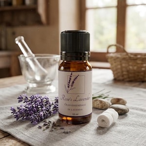 May include: A brown glass essential oil bottle with a black cap, labeled "Rose's Lavender." A sprig of purple lavender and a small roll of white cloth are on a gray linen cloth. The bottle contains 10 ml of oil.