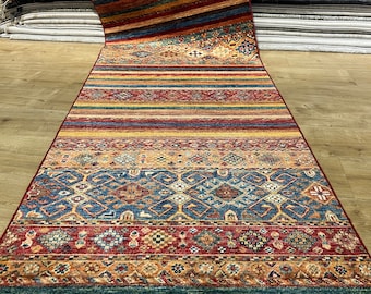 Könnte beinhalten: Ein langer, schmaler, bunter Teppich mit geometrischem Muster. Der Teppich hat unten einen Fransen und ist aus Wolle. Der Teppich ist in verschiedenen Farben, darunter Rot, Blau, Gelb und Grün.