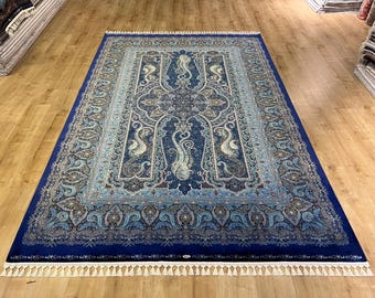 May include: A rectangular, ornate rug with a deep blue border and intricate patterns in shades of blue, beige, and white. The rug features a central medallion design and decorative fringe along the edges. The rug is displayed on a wooden floor.