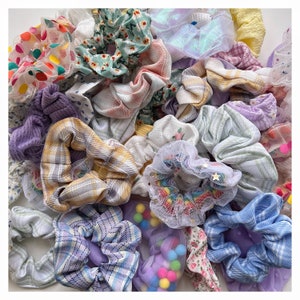 May include: A collection of colorful hair scrunchies in various patterns and textures, including plaid, floral, and mesh. The scrunchies are arranged in a pile, showcasing a variety of styles and colors.