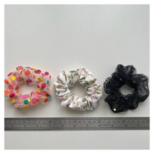 May include: Three hair scrunchies: one with pink and white polka dots, one with a floral pattern, and one black with gold stars.