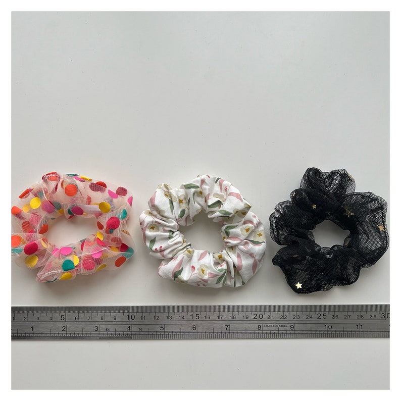 May include: Three hair scrunchies: one with pink and white polka dots, one with a floral pattern, and one black with gold stars.