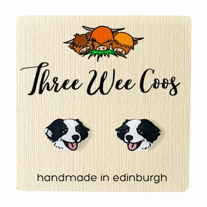 Op de afbeelding: Een paar zwart-witte oorbellen in de vorm van honden met roze tongen, gepresenteerd op een crèmekleurige kaart. De kaart bevat de tekst "Three Wee Coos" en "handmade in edinburgh", plus een cartoon van drie Schotse Hooglanders.