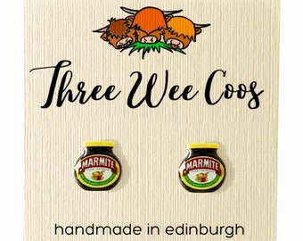 Könnte beinhalten: Ein Paar Ohrringe mit einem Cartoon-Bild eines Marmite-Glases, einem beliebten britischen Hefeextrakt-Aufstrich. Die Ohrringe sind handgefertigt in Edinburgh, Schottland. Die Karte zeigt auch ein Cartoon-Bild von drei schottischen Hochlandrindern mit dem Text "Three Wee Coo's".