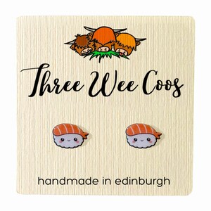 K&ouml;nnte beinhalten: Ein Paar s&uuml;&szlig;e Sushi-Ohrringe mit einem l&auml;chelnden Gesicht. Die Ohrringe sind handgefertigt in Edinburgh, Schottland. Die Ohrringe befinden sich auf einer Karte mit dem Text "Three Wee Coo's" und einem Cartoon-Bild von drei schottischen Hochlandrindern.