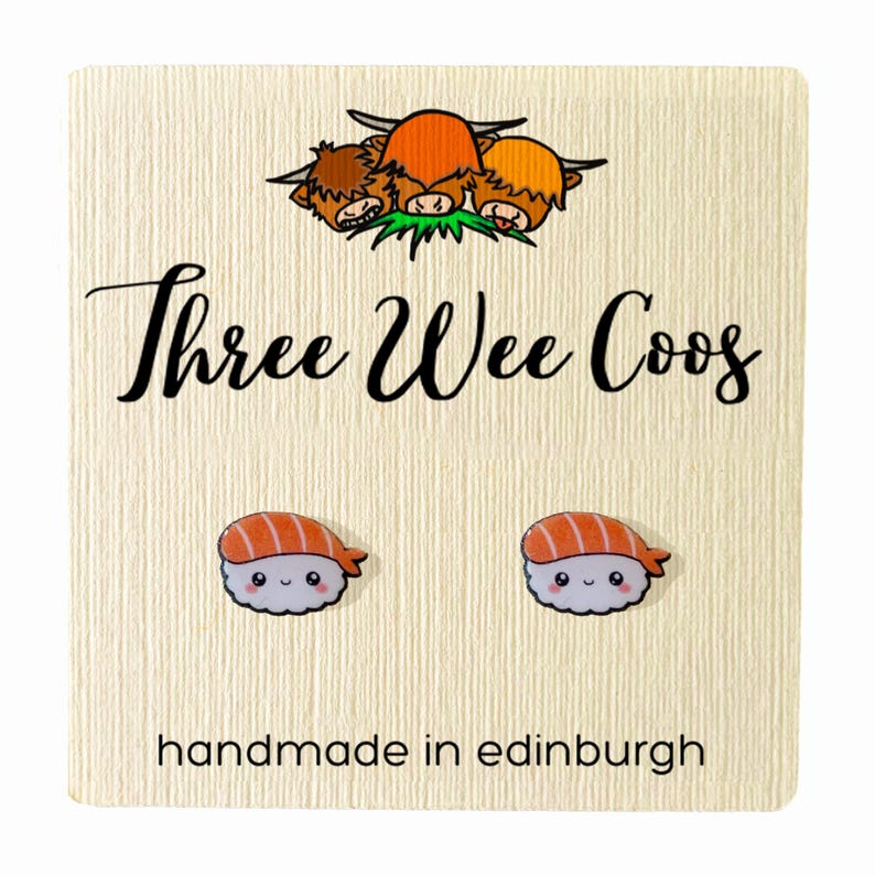 K&ouml;nnte beinhalten: Ein Paar s&uuml;&szlig;e Sushi-Ohrringe mit einem l&auml;chelnden Gesicht. Die Ohrringe sind handgefertigt in Edinburgh, Schottland. Die Ohrringe befinden sich auf einer Karte mit dem Text "Three Wee Coo's" und einem Cartoon-Bild von drei schottischen Hochlandrindern.